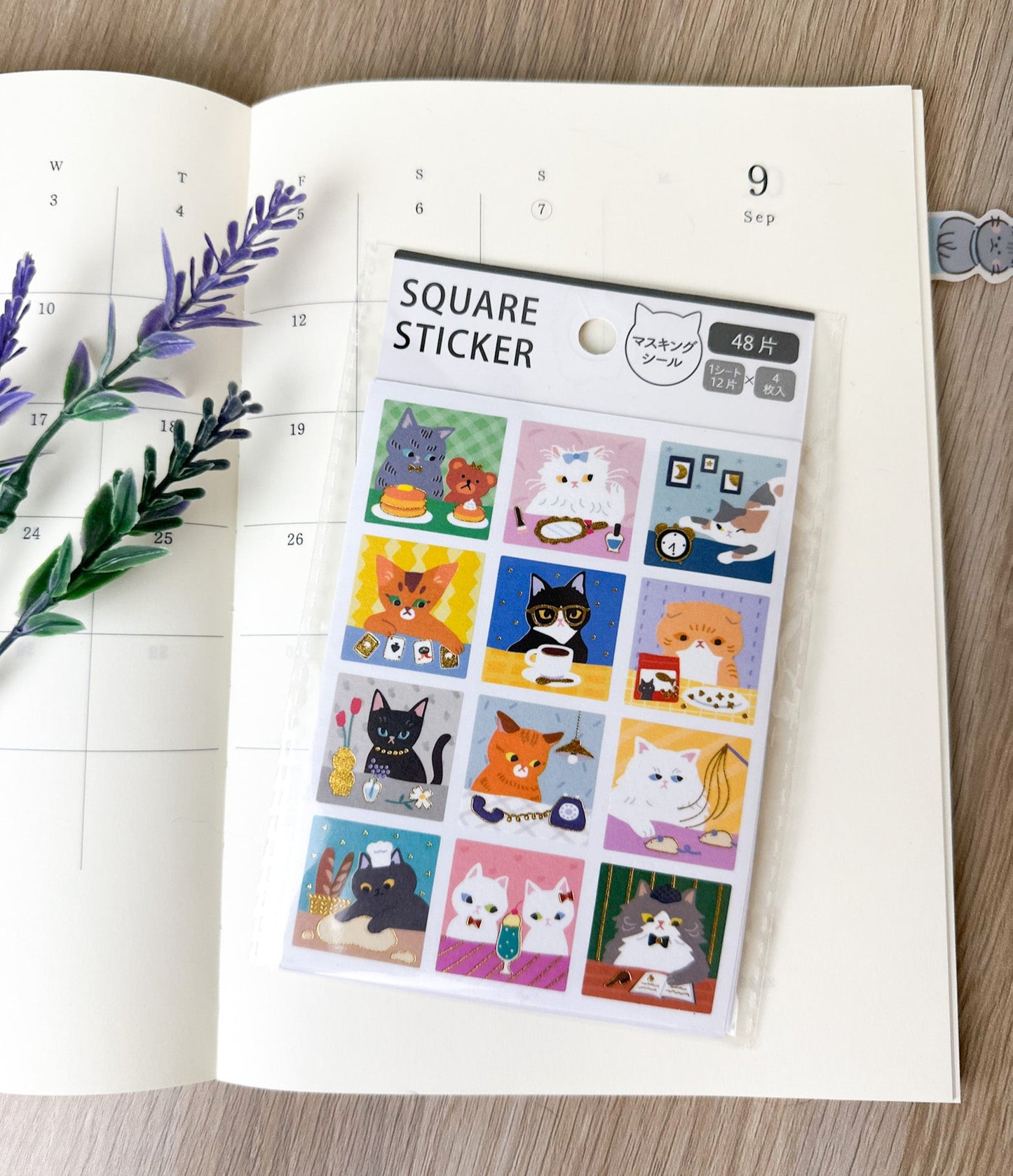 Pack de pegatinas japonesas cuadradas con gatos, colocado sobre una agenda y decoración floral