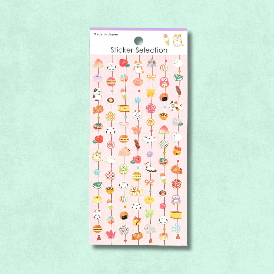 Lámina de pegatinas japonesas de Gaia con pequeños colgantes decorativos inspirados en festividades, dulces y amuletos tradicionales, en tonos alegres y detalles delicados.