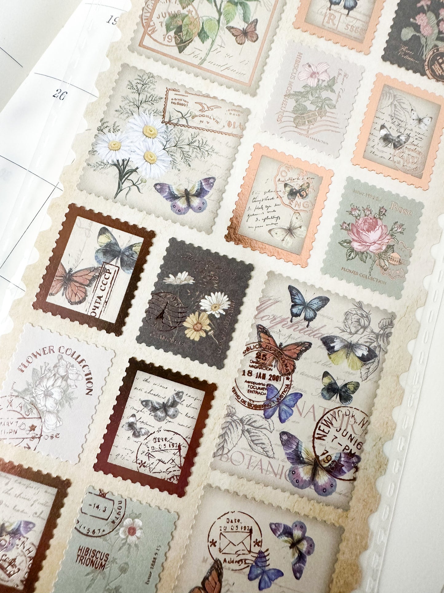 Pegatinas japonesas de mariposas y flores con estilo sello postal, colocadas sobre una agenda con decoración floral.
