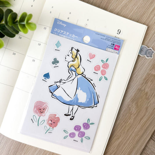 Pegatinas japonesas transparentes de Alicia en el País de las Maravillas, sobre agenda abierta con decoración de plantas.