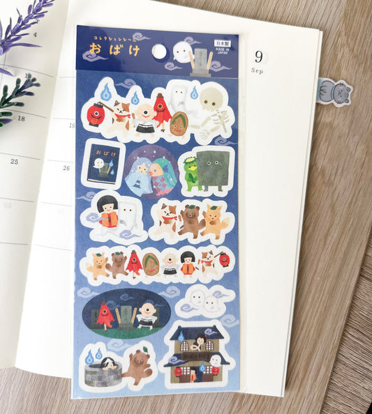 Pegatinas japonesas con ilustraciones de fantasmas y criaturas yokai sobre una agenda abierta.

