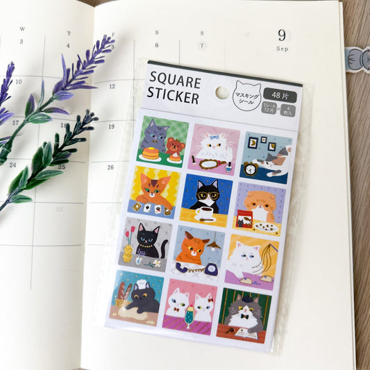 Pegatinas japonesas cuadradas con ilustraciones de gatos en diferentes escenas, sobre una agenda abierta